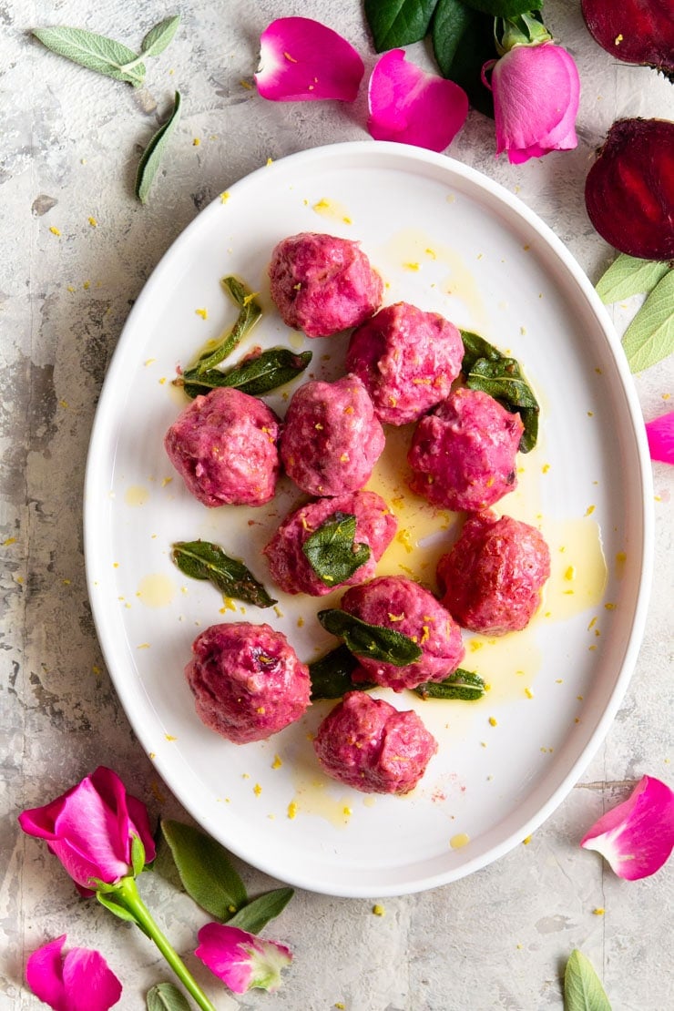 An overhead shot of beetroot ricotta gnudi on an oval plate with sage and butter