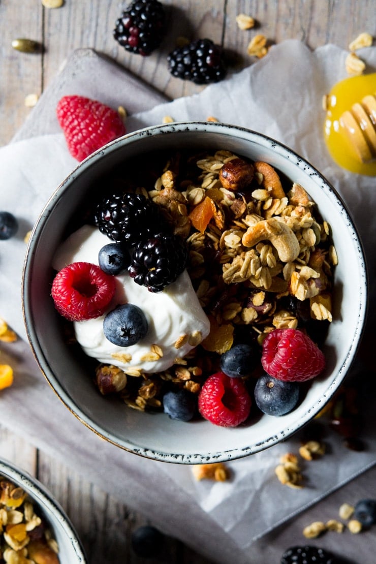 An overhead shot of healthy granola in a small bowl topped with berries and yogurt with scattered berries in the background