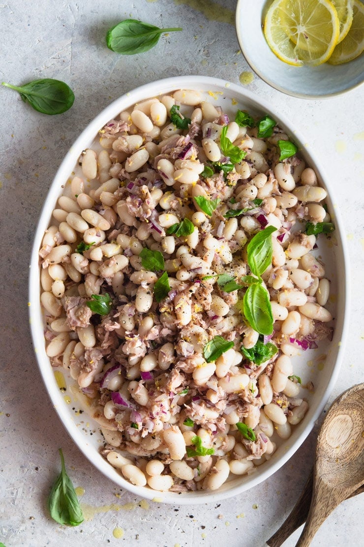 An overhead shot of a white bean salad with tuna and basil on an oval plate