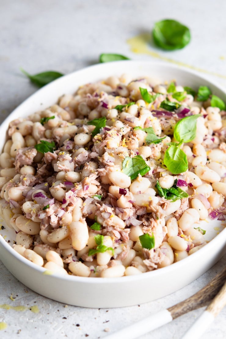 A side shot of a white bean salad with tuna and basil on a white serving plate