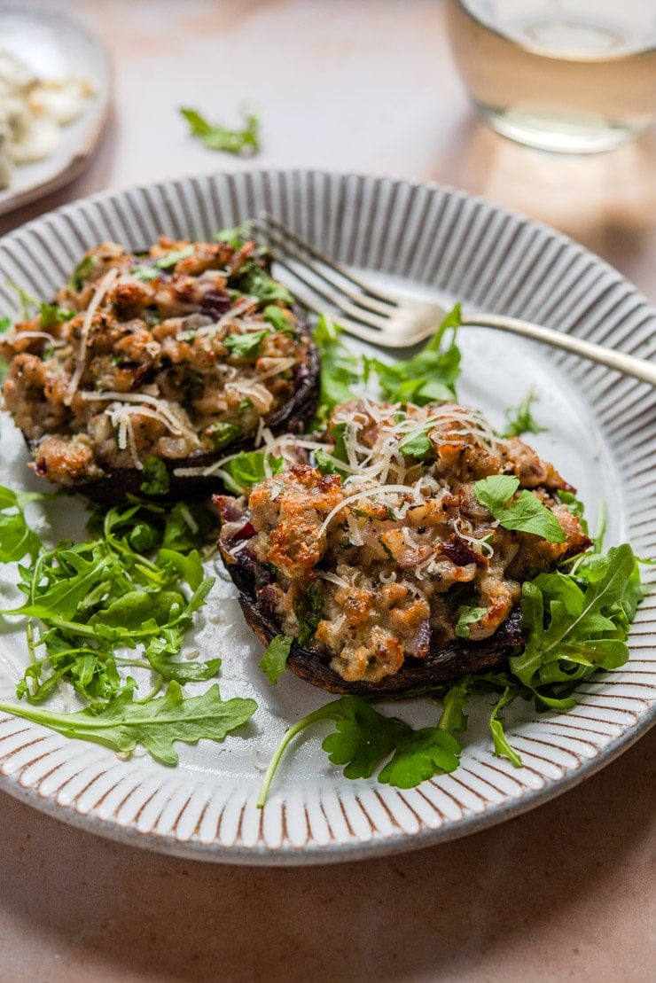 A side shot of sausage stuffed mushrooms on a plate with arugula