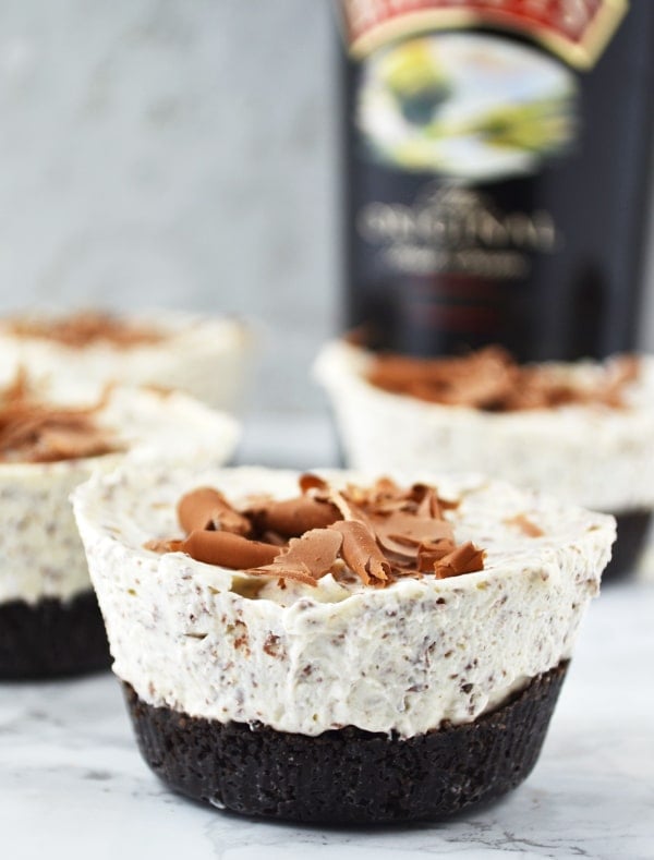 These Boozy Baileys Mini Cheesecakes are so easy to make and are the perfect festive party food, they'll be gone in no time! | Christmas Desserts | Party Food | A close up of baileys cheesecakes with a bottle of baileys in the background