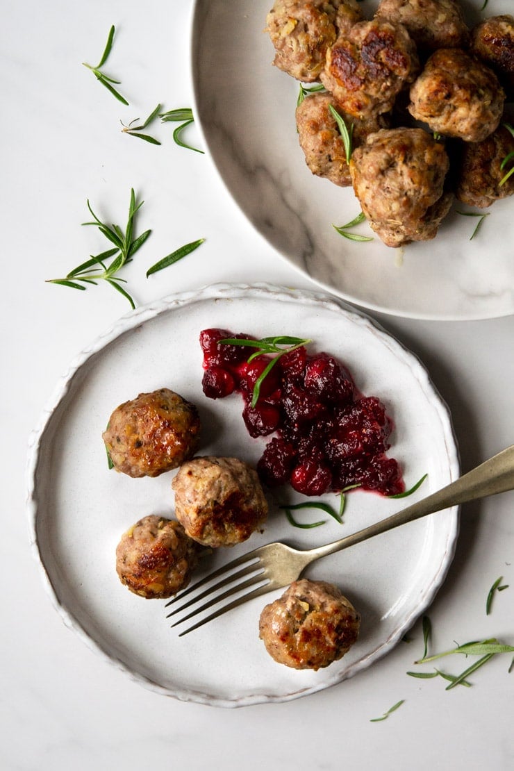 Sausage stuffing balls on a plate with cranberry sauce and fresh rosemary