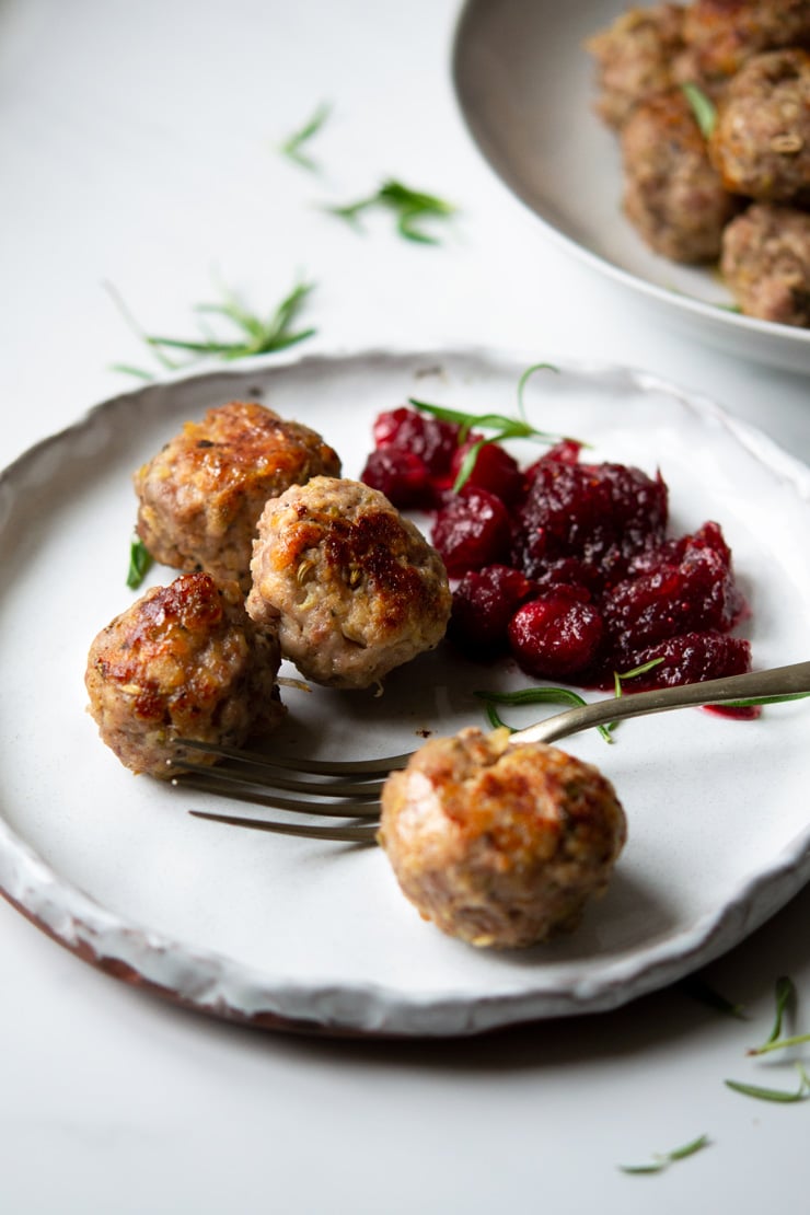 A close up of sausage stuffing balls on a plate with cranberry sauce