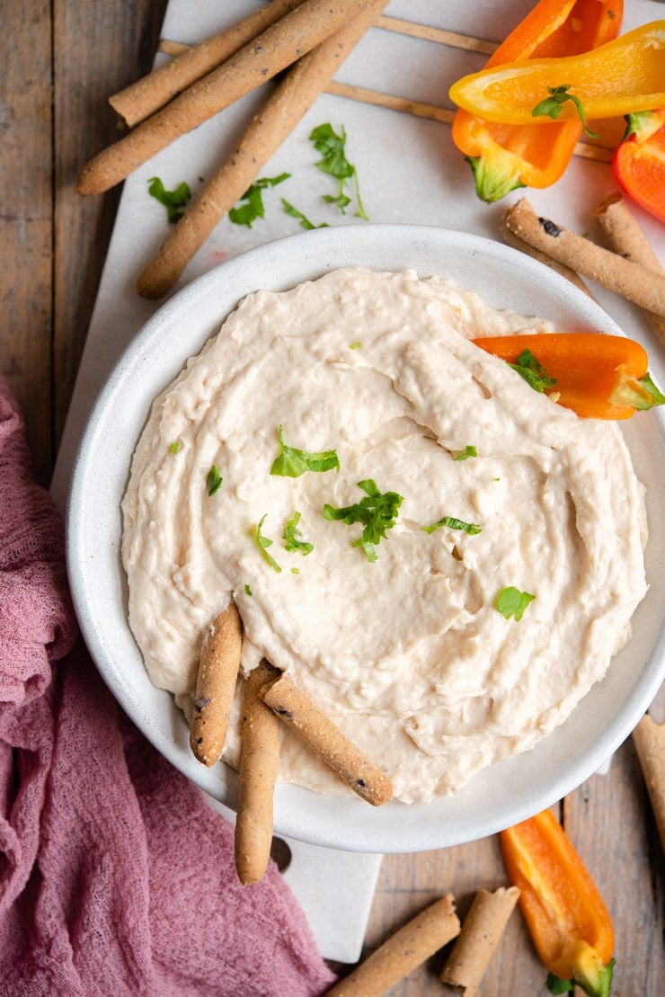 An overhead shot of a creamy bean dip with breadsticks and veggies around it