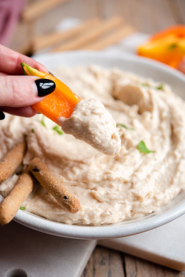 A close up of dipping bell peppers into a white bean dip