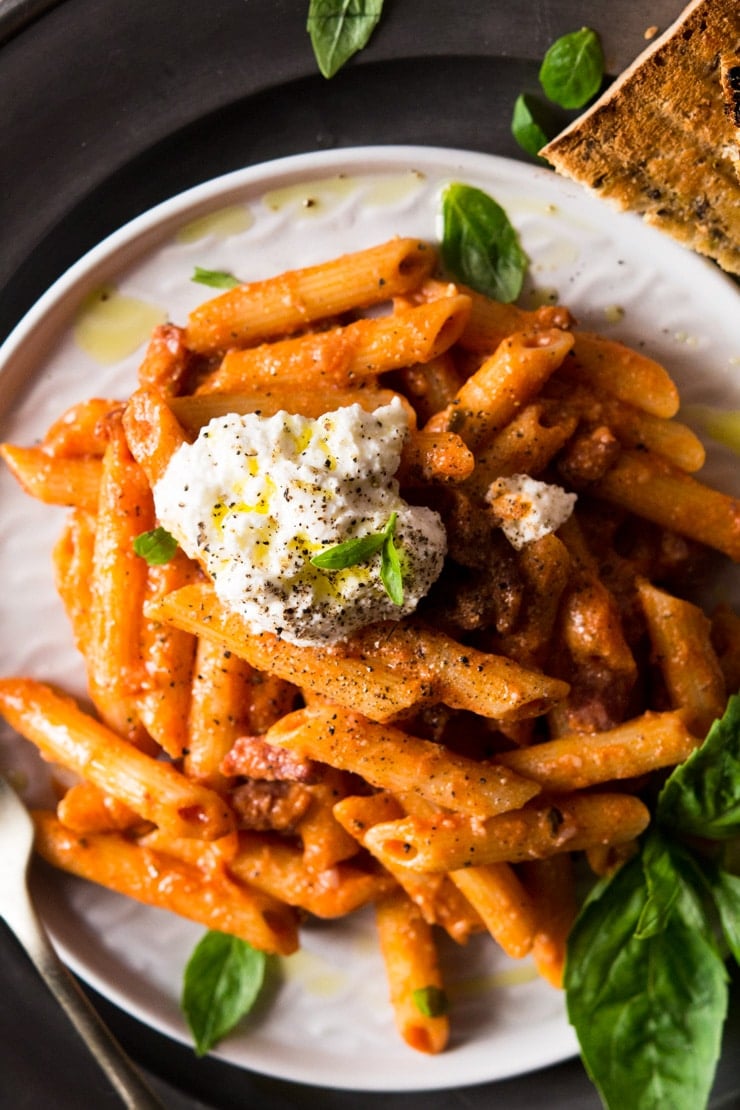 A close up of pasta with pancetta topped with a dollop of ricotta cheese