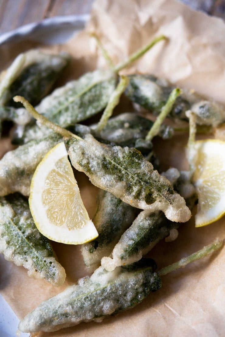 A close up of fried sage leaves in a plate with lemon wedges