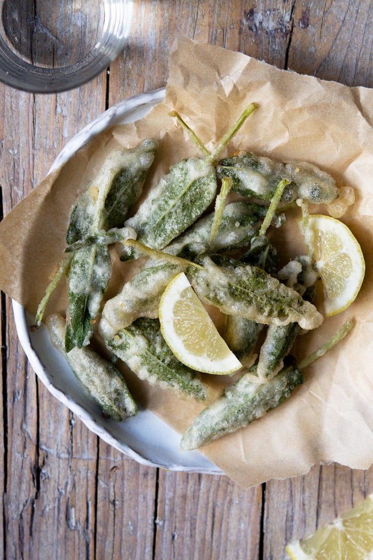 An overhead shot of fried sage leaves stuffed with anchovies on a plate with lemon wedges