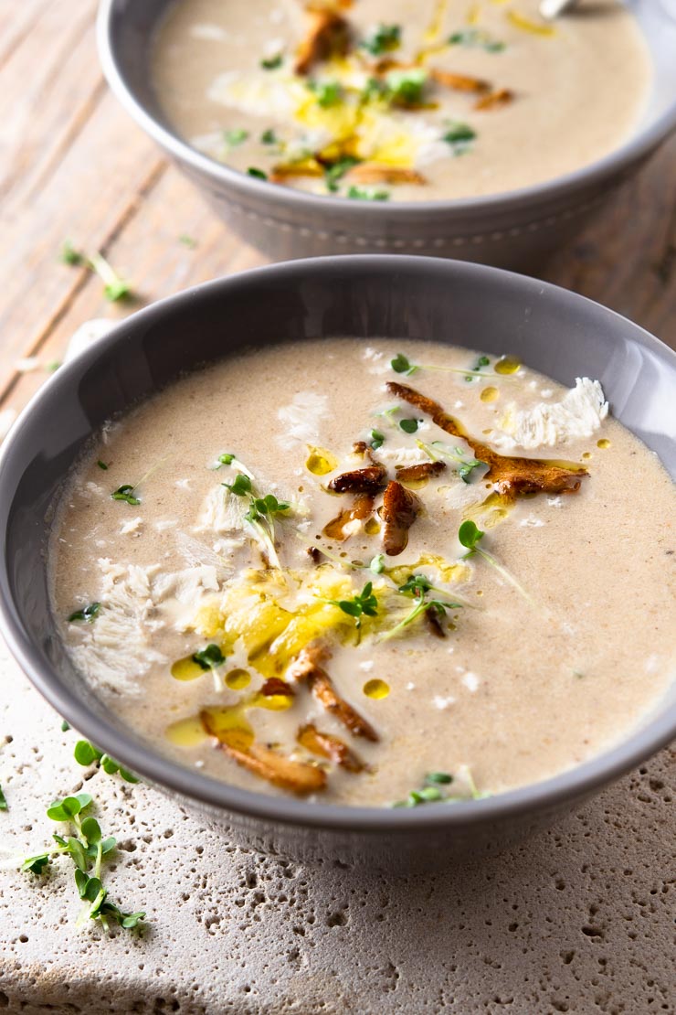 A close up of a bowl of creamy mushroom soup topped with mushrooms and olive oil