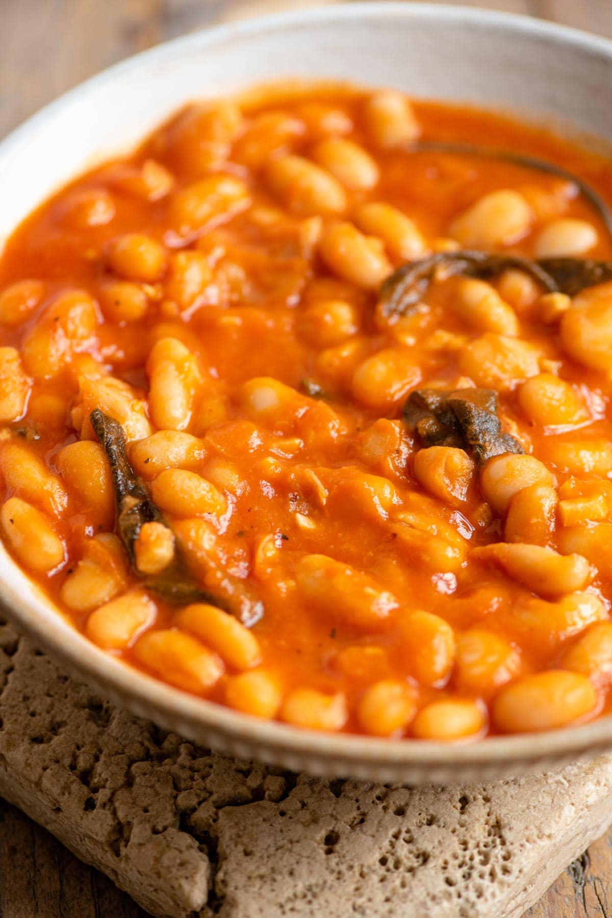 A close up of a bowl of beans in tomato sauce with sage leaves