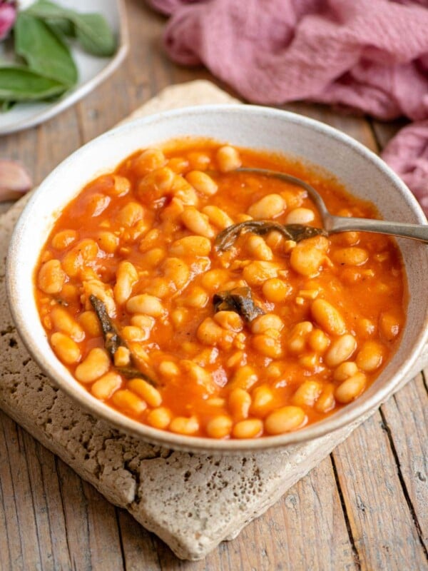 A bowl of cannellini bean in tomato sauce with sage sitting on a wooden surface