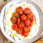 A square image of a ricotta dip in a bowl topped with tomatoes