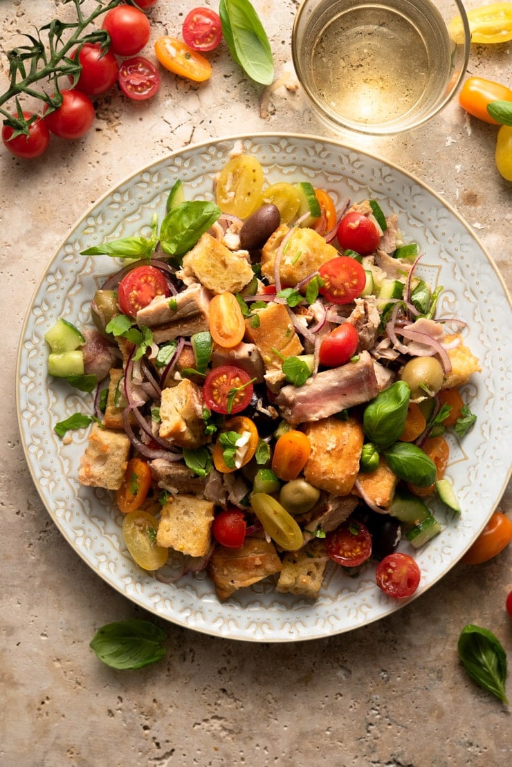 An overhead shot of a tuna panzanella salad on a large plate with tomatoes and basil scattered around