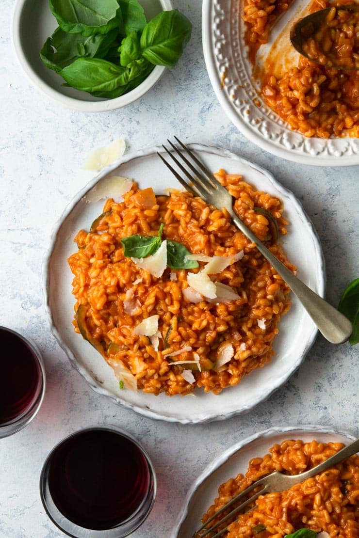 An overhead shot of tomato risotto on a plate topped with parmesan and basil