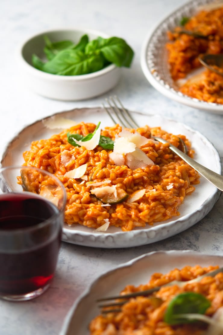 A plate of tomato risotto with a fork and a glass of red wine at the side