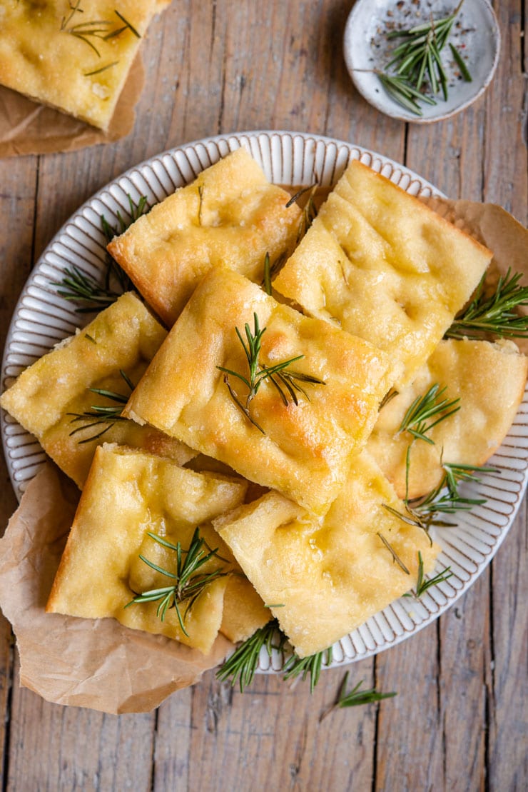 A classic Rosemary Focaccia Bread made with simple pantry ingredients. This traditional Italian focaccia is absolutely delicious served as it is or can be used to make sandwiches, dunk into a hot bowl of soup or get adventurous and try out different toppings. #focaccia #bread #Italianrecipes An overhead shot of rosemary focaccia on a plate