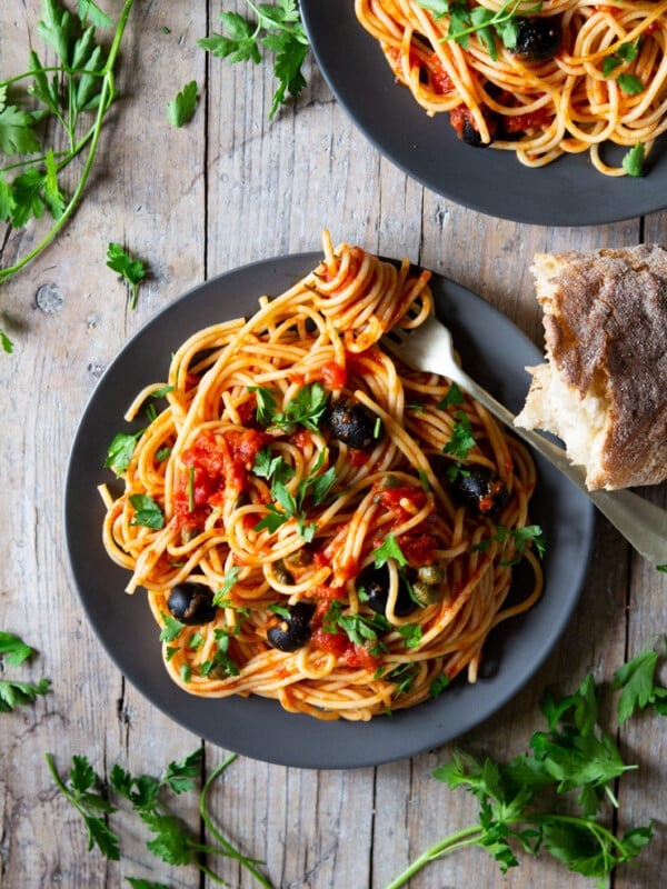 A plate of spaghetti with puttanesca sauce sitting on a wooden surface