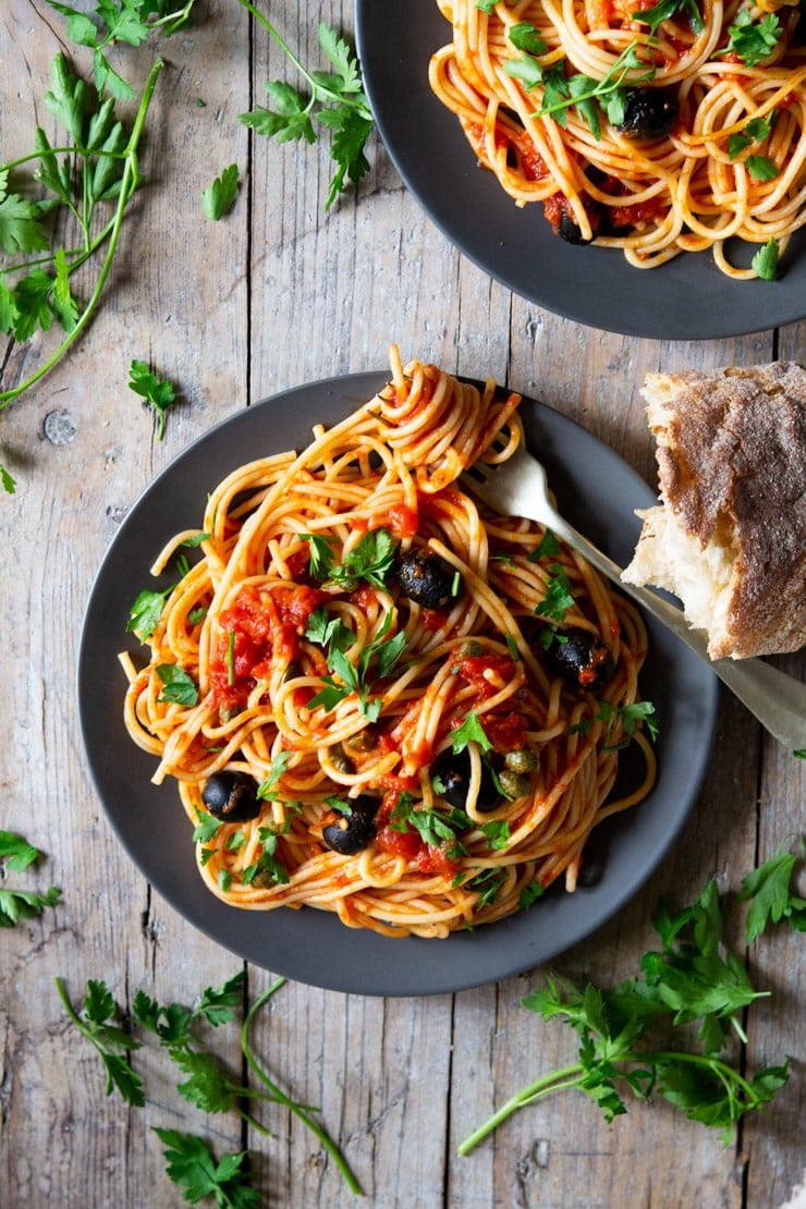 A plate of spaghetti with puttanesca sauce sitting on a wooden surface