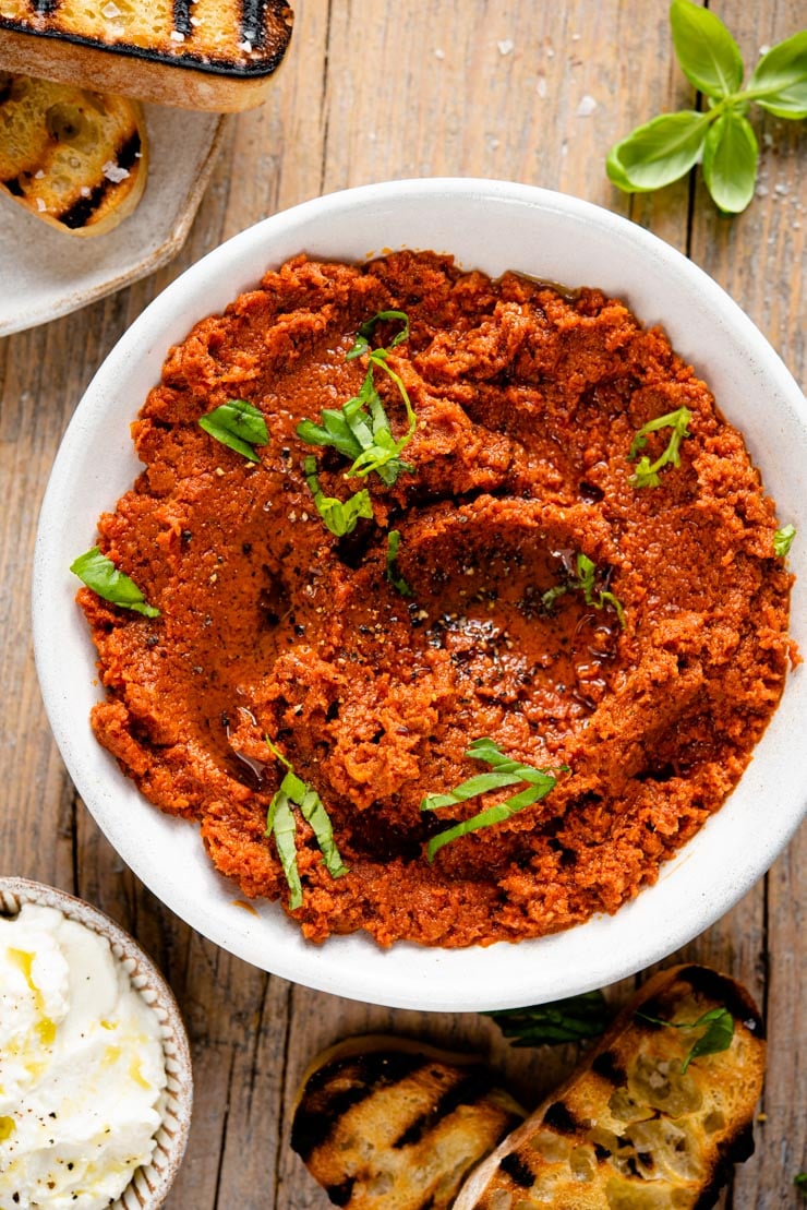 Red pesto in a bowl with basil and bread at the side