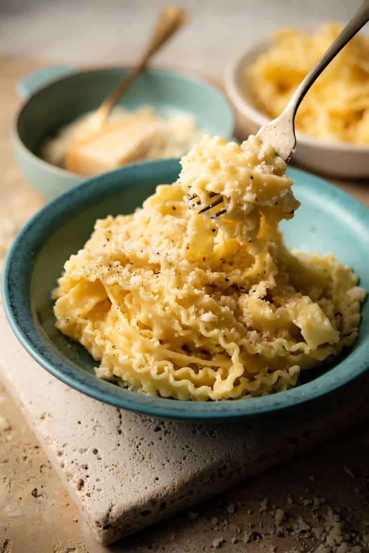 A fork picking up some parmesan pasta from a bowl