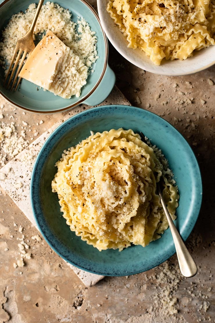 An overhead shot of two bowls of parmesan pasta with grated parmesan in a bowl at the side