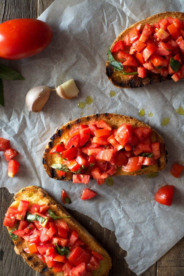 Three slices bruschetta al pomodoro - of char grilled crusty bread with chopped fresh tomatoes on top sitting on a wooden surface