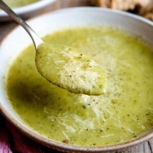 A close up of a spoonful of zucchini potato soup topped with parmesan.