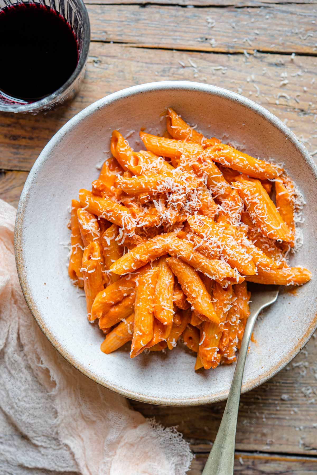 An overhead shot of penne alla vodka in a rustic bowl with a glass of red wine at the side