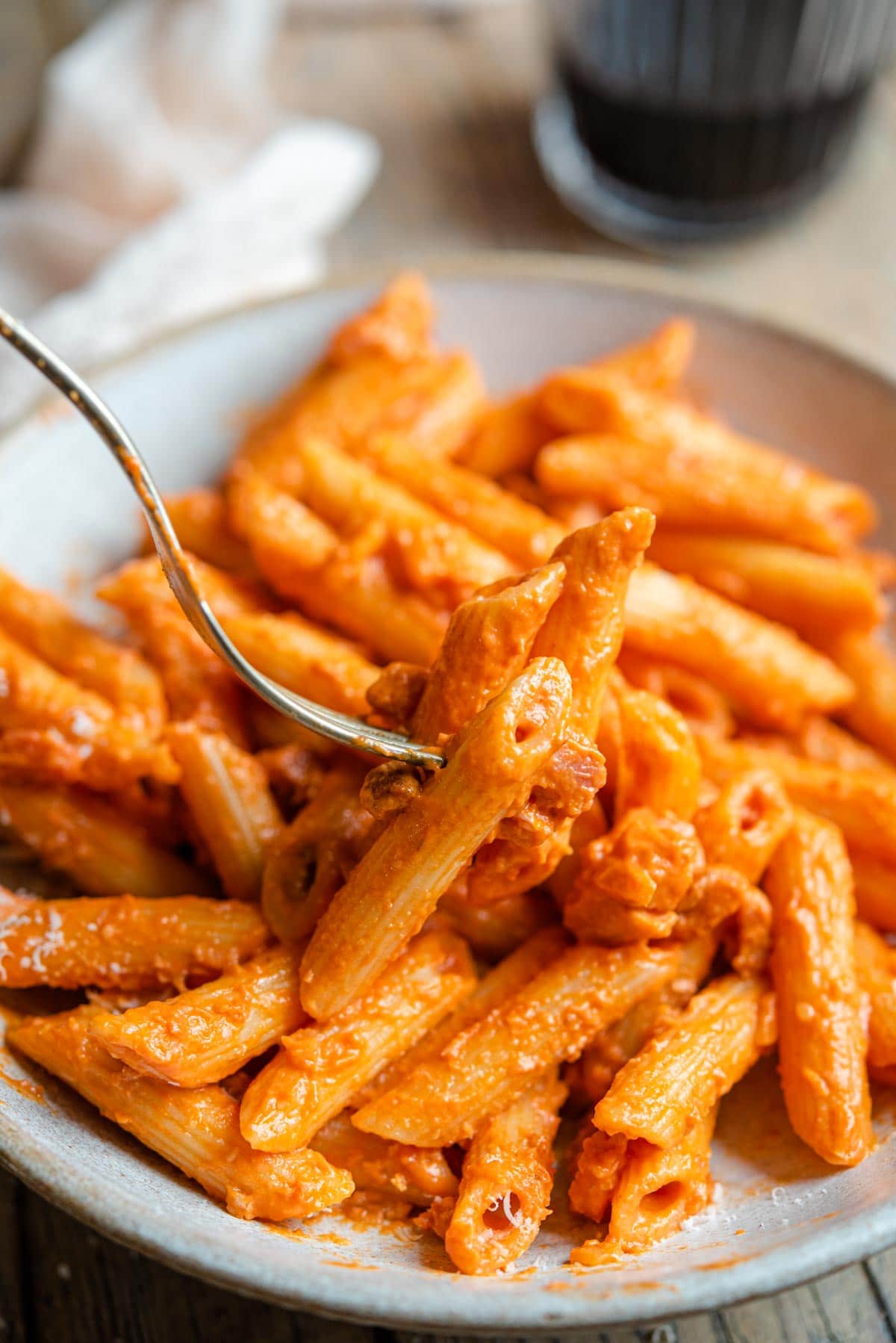 A close up of a fork picking up pasta with a tomato vodka sauce