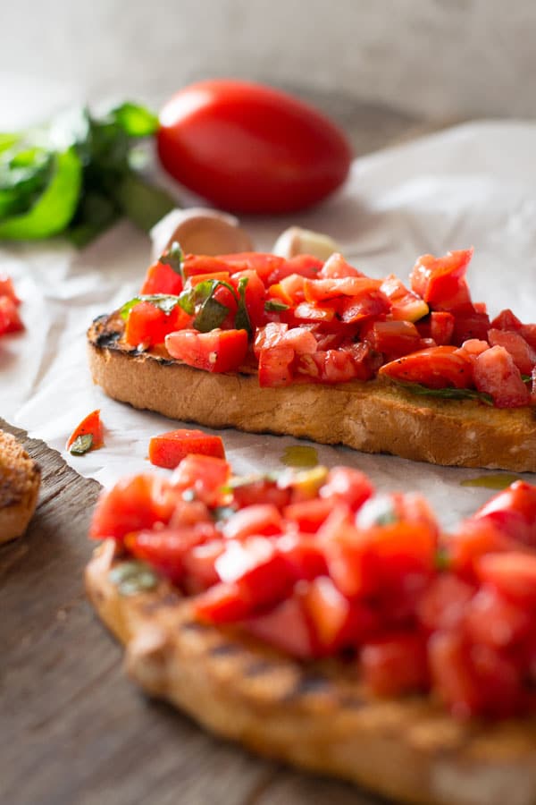 A close up of chopped fresh tomatoes on toasted garlic bread sitting on a wooden board