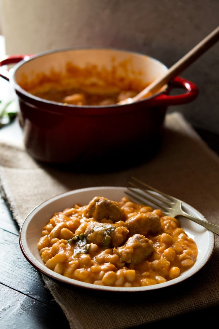 A close up of Tuscan bean stew with sausages on a plate with a fork, pot in the background.