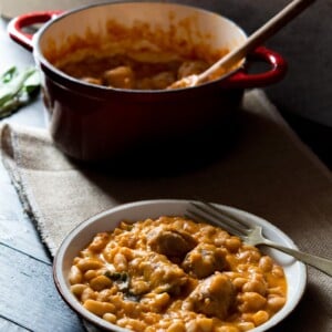 Tuscan bean stew with sausages on a plate, fork at the side and pot in the background