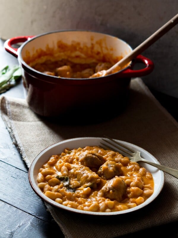 Tuscan bean stew with sausages on a plate, fork at the side and pot in the background