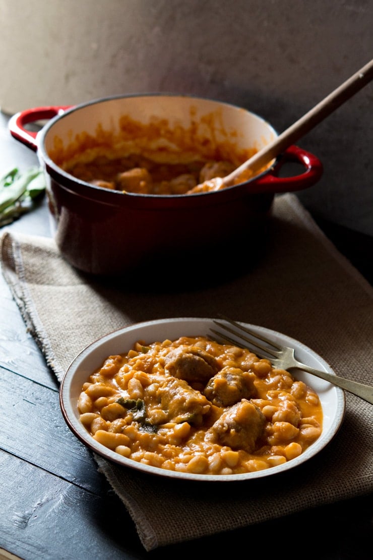 Tuscan bean stew with sausages on a plate with a fork at the side and a pot in the back ground