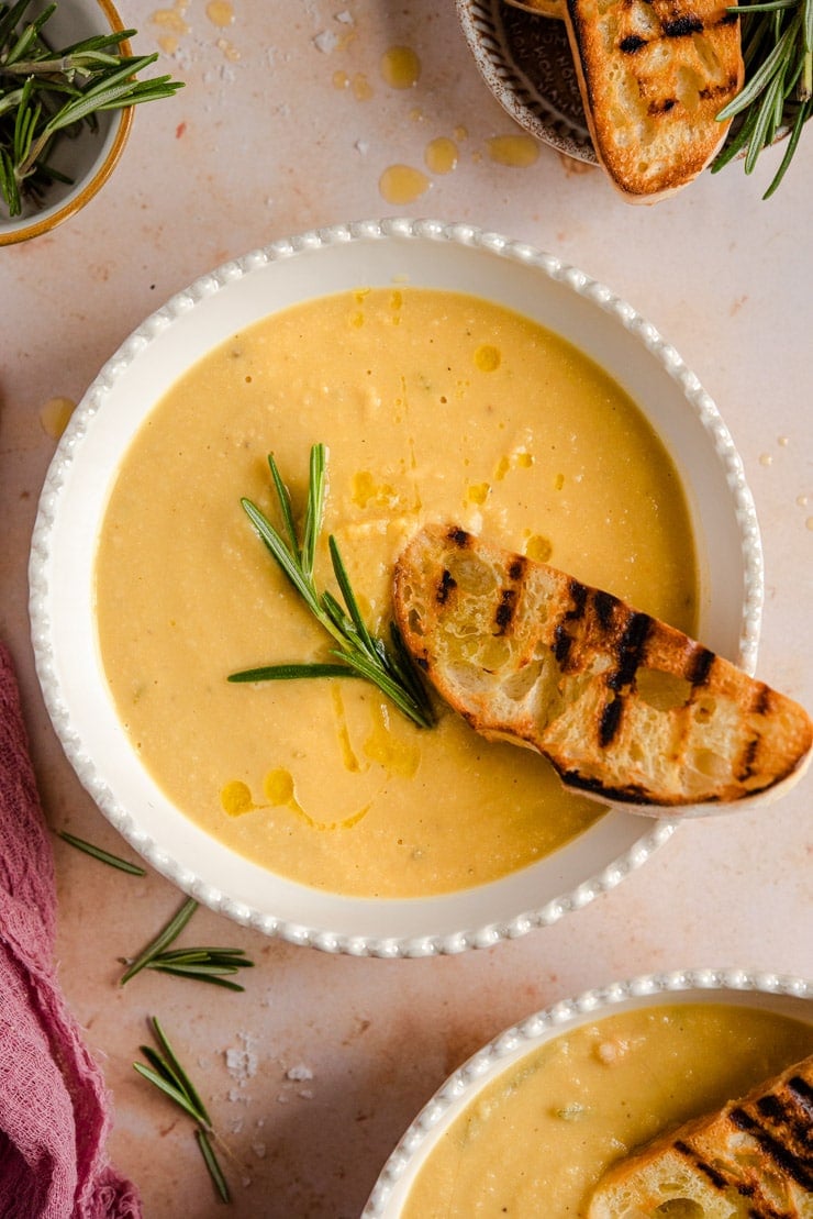 An overhead shot of chickpea soup in a bowl topped with a sprig of rosemary