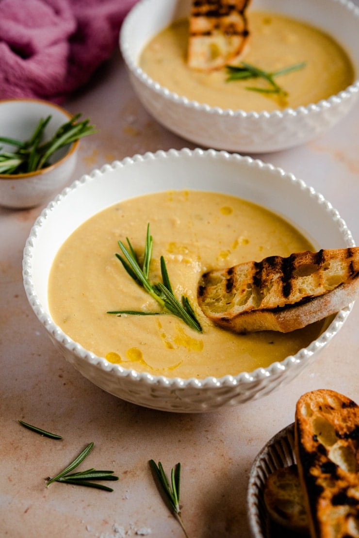 A side shot of chickpea soup in a bowl topped with crusty bread