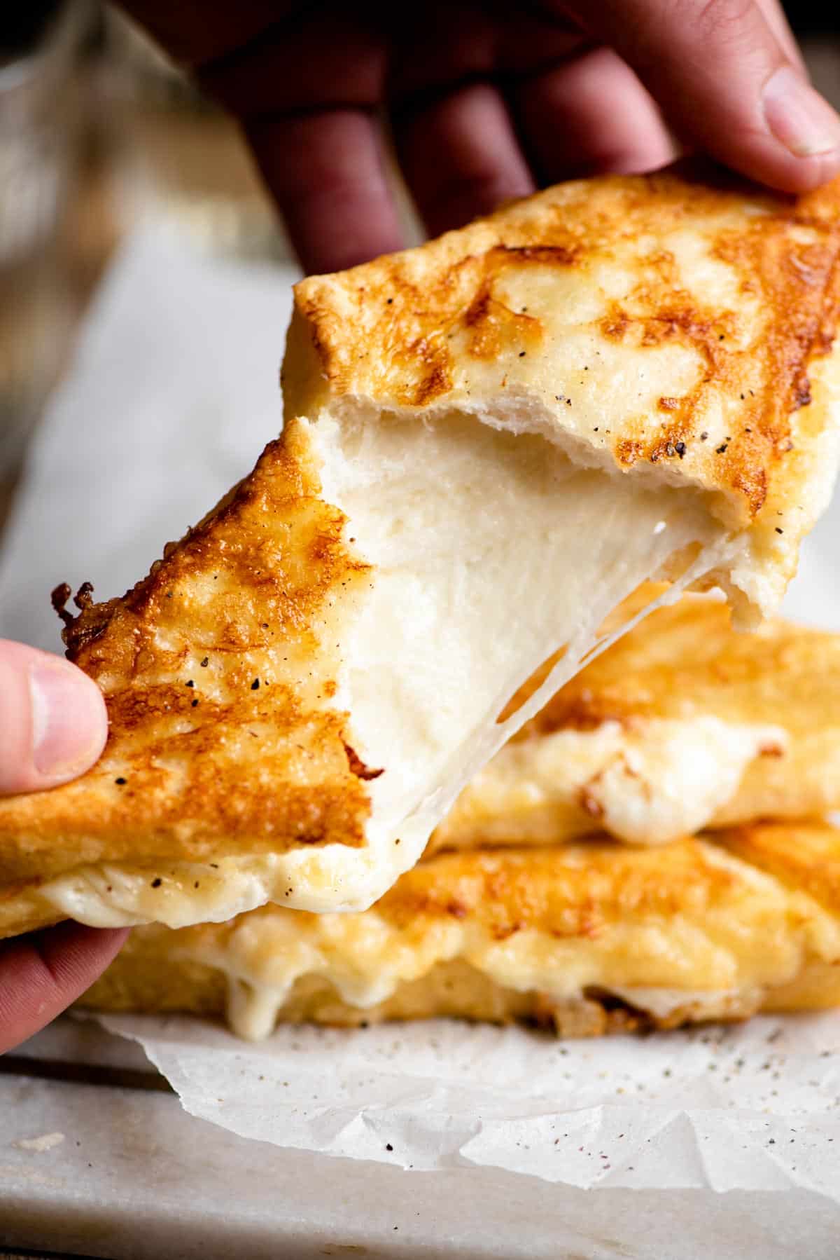 A close up of a fried mozzarella sandwich broken open with cheese oozing and stretching