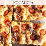 Tomato and anchovy focaccia cut into slices lying on a travertine surface.