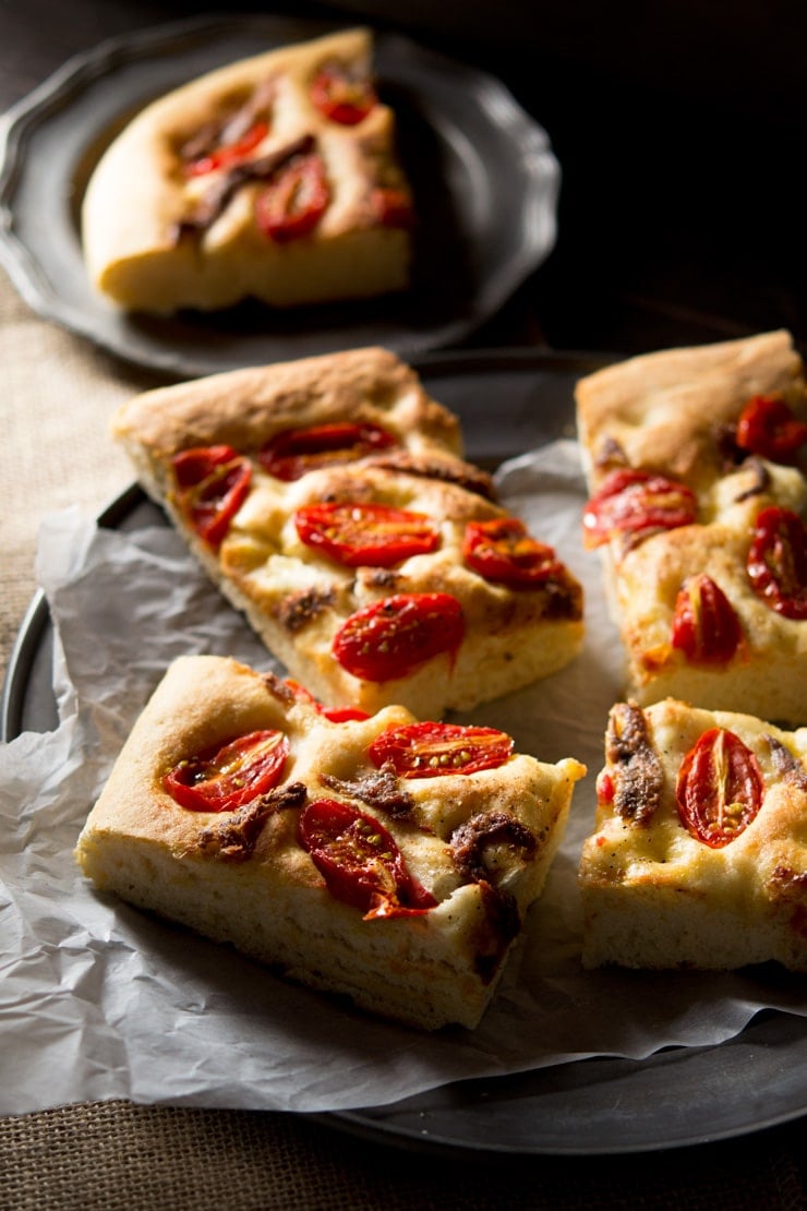 Cherry tomato focaccia with anchovies cut into slices sitting on a rustic plate