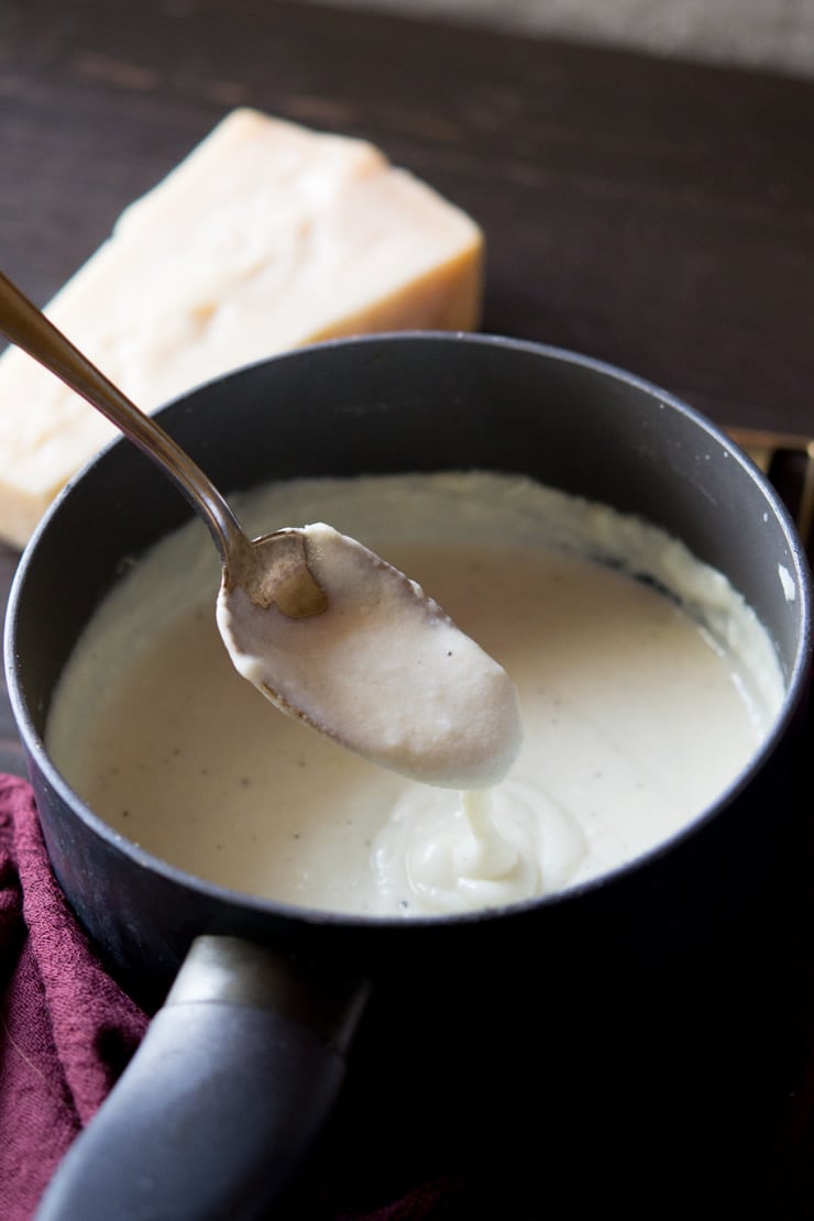 A close up shot of bechamel sauce in a saucepan with parmesan in background - how to make bechamel sauce recipe