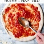 A Pinterest graphic showing a hand spreading tomato sauce on pizza dough sitting on a marble surface.