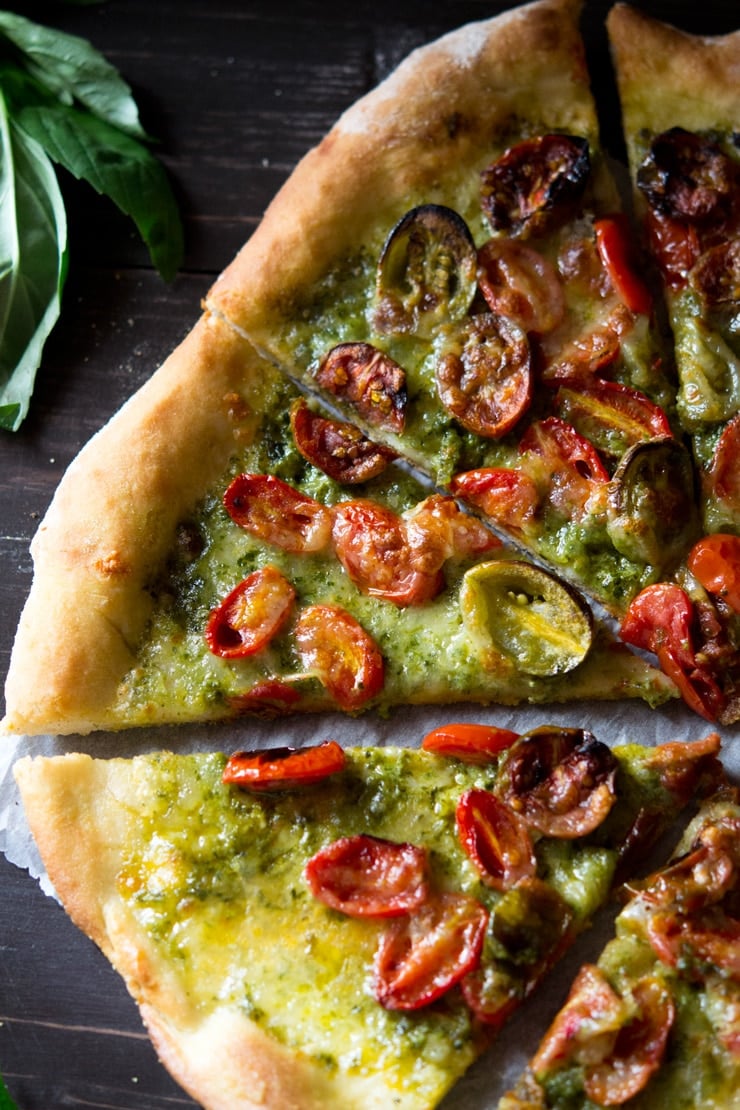 A close up shot of a slice of basil pesto pizza with basil in the background