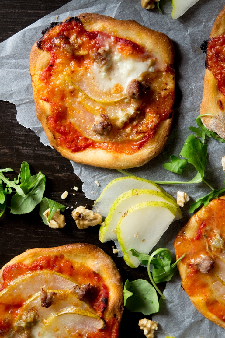 A close up of mini sausage pizzas with arugula, walnuts and pear beside it
