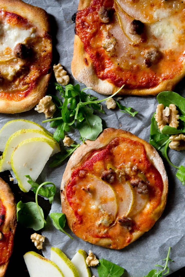 An overhead photo of mini sausage pizzas with pear, gorgonzola and arugula