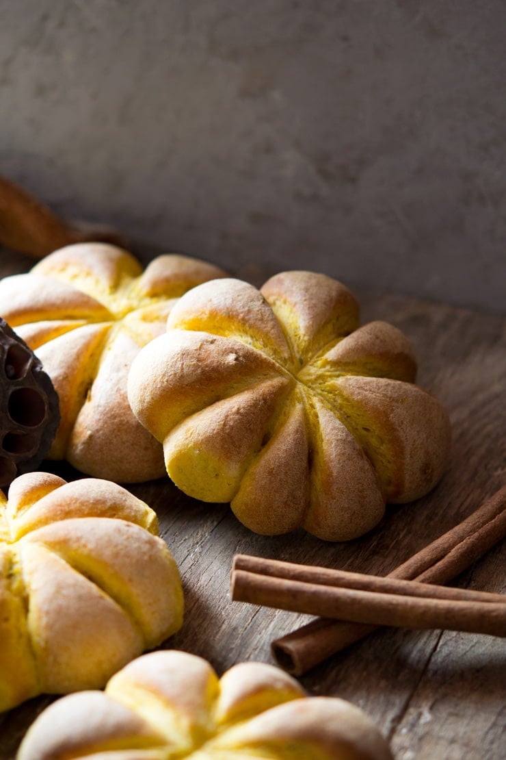 Pumpkin bread rolls sitting on a wooden surface (the rolls are pumpkin shaped)