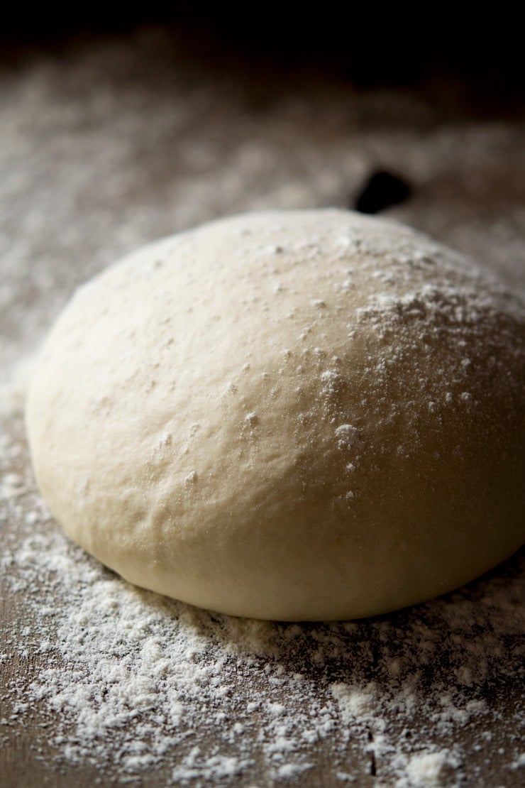 A close up of the best basic pizza dough recipe in a ball on a floured work surface