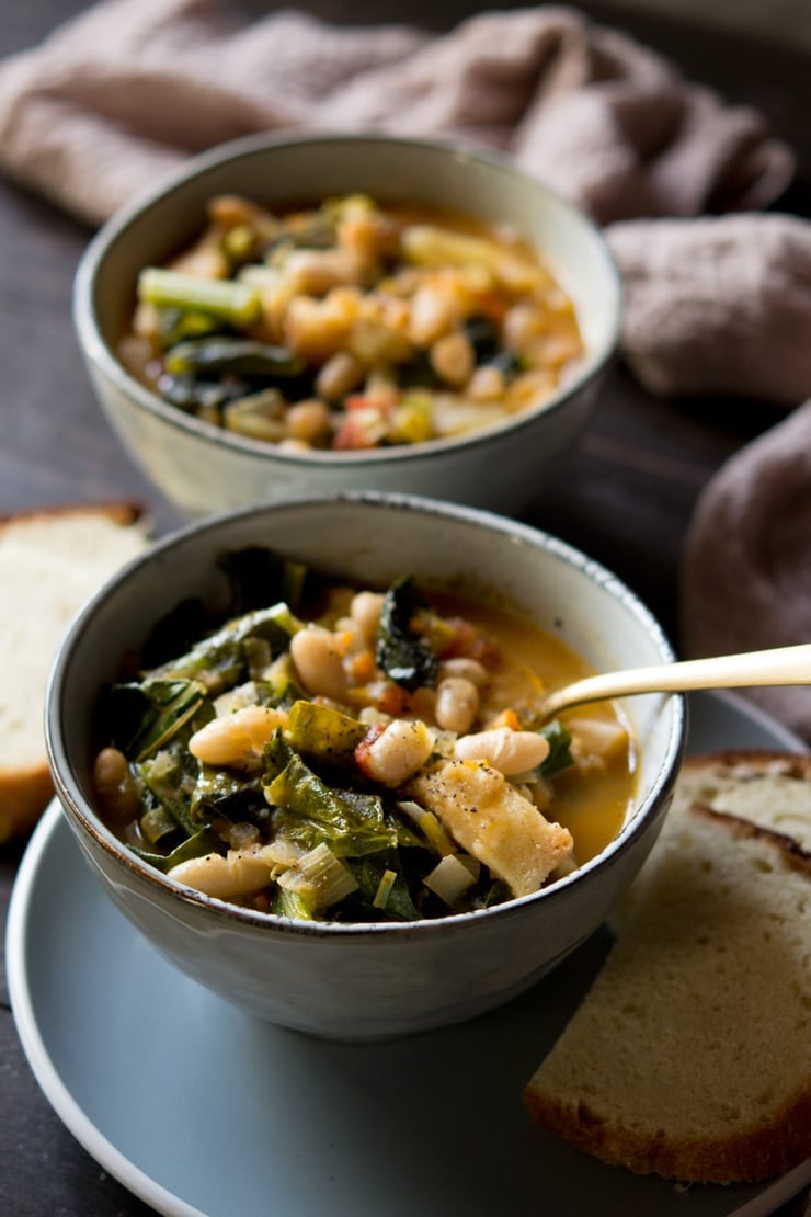 close up of a bowl of Tuscan vegetable soup another bowl with bread in back ground