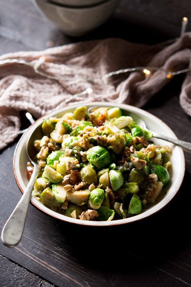 sauteed brussels sprouts with dates and walnuts on a serving plate with spoons