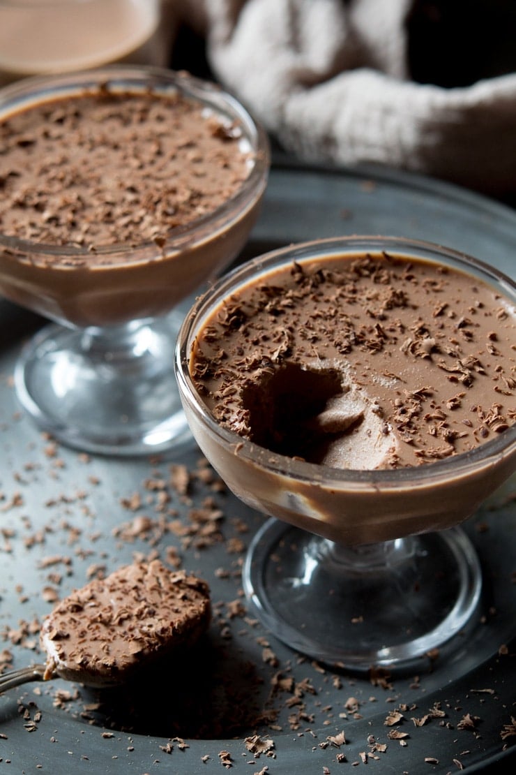 A close up of chocolate panna cotta with a spoonful of panna cotta in the background